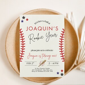 May include: Baseball-themed birthday party invitation with red stitching, a baseball, and a bat. The invitation reads "Let's have a ball at Joaquin's Rookie Year. Please join us to celebrate Joaquin is turning one! Feb 27, 2-4 PM. At the Chester Fields, 123 Anystreet, Any City, CA. RSVP to Melissa 123.456.7891."
