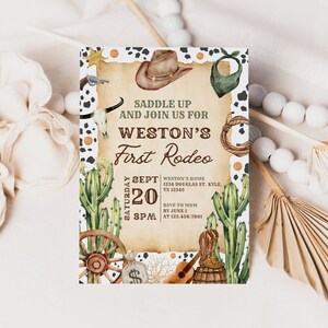 K&ouml;nnte beinhalten: Eine rustikale Einladung zu einer ersten Rodeo-Party. Die Einladung zeigt einen Cowboyhut, einen Kaktus, ein Wagenrad und eine Gitarre. Der Text auf der Einladung lautet "Saddle Up and Join Us for Weston's First Rodeo, Saturday Sept 20, 8PM, Weston's Home, 1234 Douglas St. Kyle, TX 12345, RSVP to Mom by June 1 at 123.456.7891".