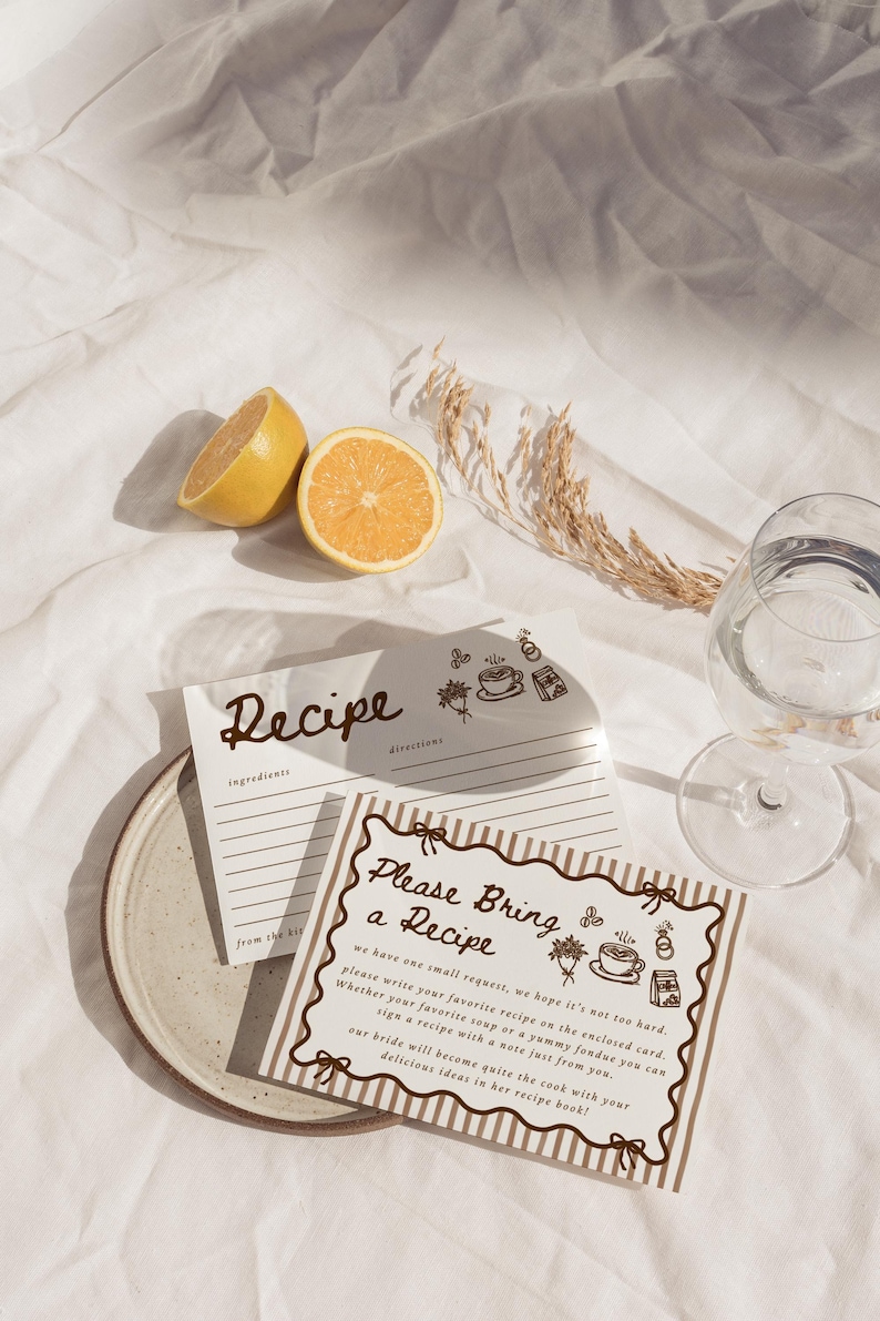 Peut inclure: Nature morte avec des cartes de recettes, une assiette, un verre d'eau et des citrons coup&eacute;s en deux sur un tissu blanc. Les cartes de recettes portent les mentions "Recipe" et "Please Bring a Recipe".