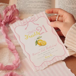 May include: A rectangular birthday invitation card with deckled edges, featuring a pink striped border, a bow illustration, and a lemon graphic. The text reads: She's Freshly 21, Bianca 21st Birthday, 12.10.2024 at 4 PM, The Fizzy Bar, 123 any street, any state, 12345, Rsvp to Bianca at 123.456.7891.