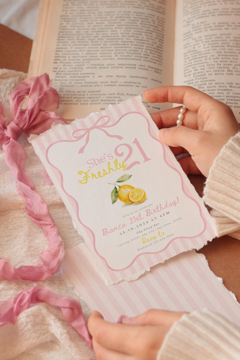 May include: A rectangular birthday invitation card with deckled edges, featuring a pink striped border, a bow illustration, and a lemon graphic. The text reads: She's Freshly 21, Bianca 21st Birthday, 12.10.2024 at 4 PM, The Fizzy Bar, 123 any street, any state, 12345, Rsvp to Bianca at 123.456.7891.