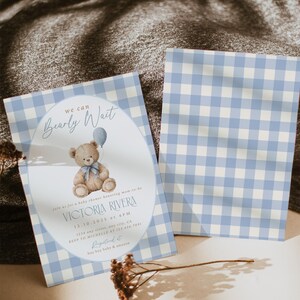 May include: Baby shower invitation featuring a teddy bear holding a blue balloon. The invitation has a light blue and white gingham pattern. Text includes "Bearly Wait" and details for Victoria Rivera's baby shower.