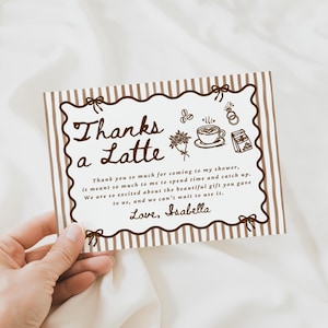 Peut inclure: Une tasse en c&eacute;ramique blanche avec une anse noire et le texte "But First, Coffee" en noir. La tasse, remplie d'un liquide fonc&eacute;, repose sur une surface en bois.