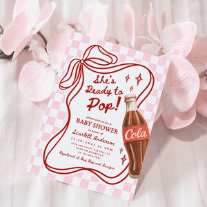 Puede incluir: Una invitaci&oacute;n para baby shower con un dise&ntilde;o retro. La invitaci&oacute;n presenta el texto "She's Ready to Pop!" en rojo, junto con una ilustraci&oacute;n de una botella de cola de dibujos animados. El fondo tiene un patr&oacute;n de cuadros rosas y blancos, y la invitaci&oacute;n est&aacute; rodeada de flores rosas.