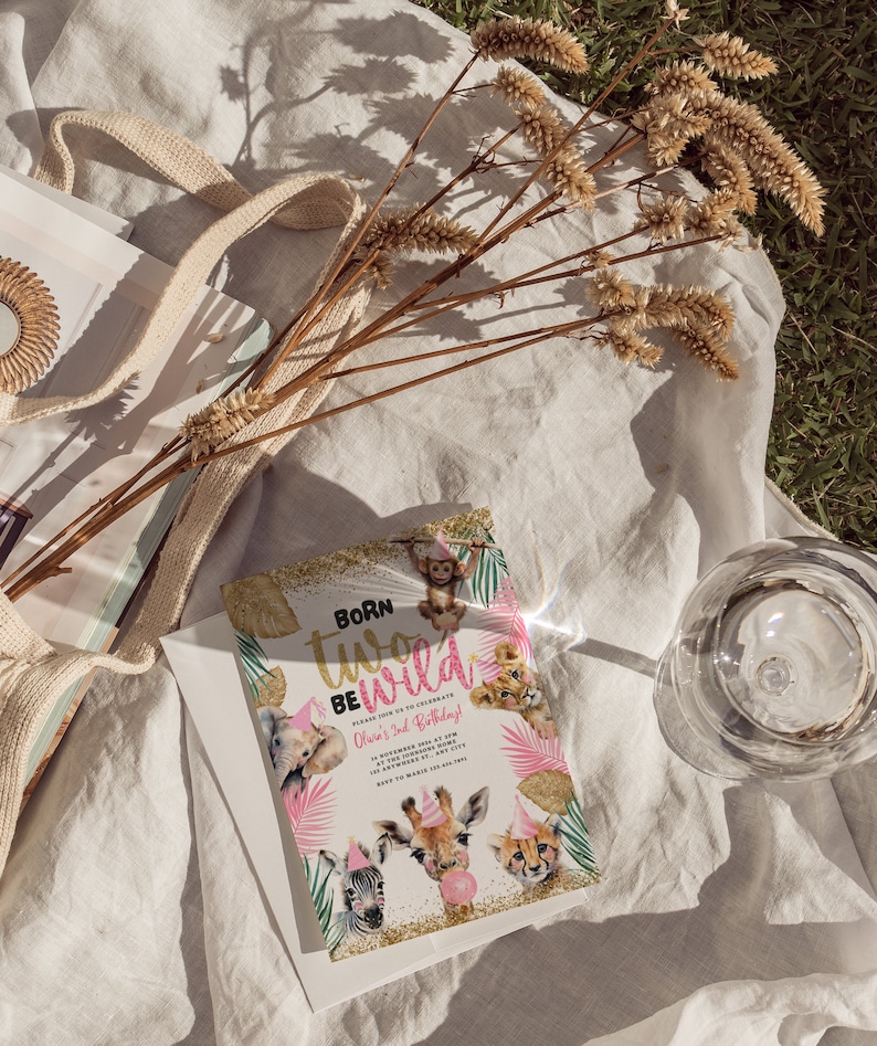 Op de afbeelding: Een verjaardagsuitnodiging met de tekst "Born Two Be Wild" met illustraties van safaridieren. De uitnodiging staat op een witte envelop, met een beige draagtas en gedroogde bloemen op de achtergrond.
