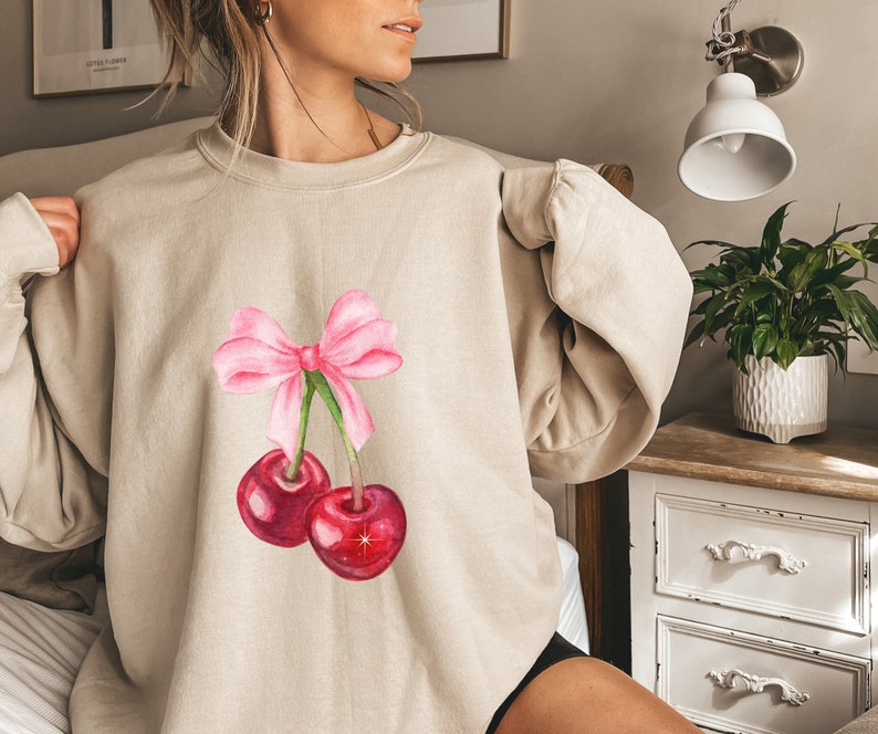 May include: A beige sweatshirt with a pink bow and two red cherries on the front.
