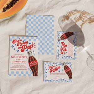 Może przedstawiać: Zestaw papeterii na baby shower z motywem butelki coli w stylu retro. Zaproszenie głosi "She's Ready to Pop" z niebiesko-białym wzorem w kratkę. Plasterek papai widoczny jest w lewym g&oacute;rnym rogu.