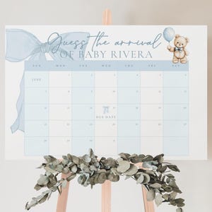May include: A blue and white calendar with a blue bow and a teddy bear holding a balloon. The calendar is for guessing the arrival of baby Rivera. The calendar has the months of June and July.