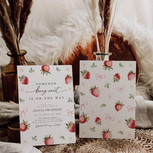 May include: A baby shower invitation with a watercolor illustration of strawberries and pink bows. The text reads "Someone berry sweet is on the way" and includes the name Olivia Swanson, the date and time of the shower, and the location.