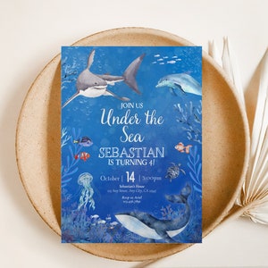 May include: An invitation with an underwater theme. The blue background features illustrations of a shark, dolphin, and various fish. Text reads "Join Us Under the Sea, Sebastian is turning 41, October 14, 3:00pm."