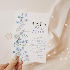 Puede incluir: Una invitaci&oacute;n a un baby shower con un dise&ntilde;o floral de acuarela en tonos azules. La invitaci&oacute;n dice "Baby in Bloom" e incluye los detalles del evento, como la fecha, la hora, el lugar y la informaci&oacute;n de RSVP.