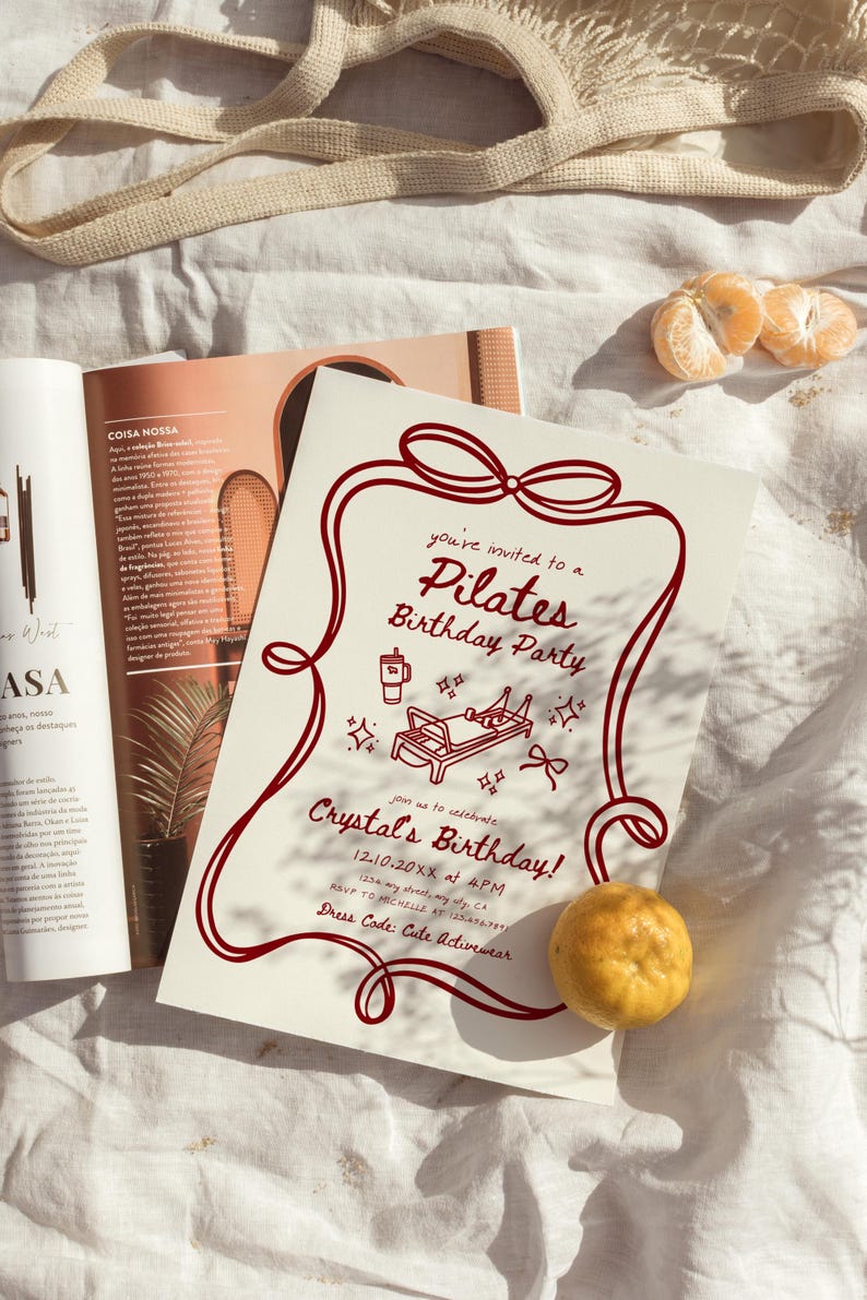 May include: A Pilates birthday party invitation with a burgundy border and text. The invitation includes illustrations of Pilates equipment and a coffee cup. A mandarin orange and a magazine are also visible.