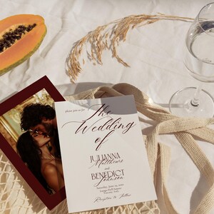 May include: Wedding invitation with the text "The Wedding of Julianna Matthews and Benedict Johnsen". The invitation is on a white background with a photo of a couple kissing. A half papaya and a glass of water are also visible.
