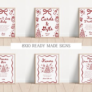 May include: Six framed signs with red and white Christmas-themed illustrations and text. The signs include phrases like "Don't Say Baby," "Cards & Gifts," and "Family Traditions." The signs are 8x10 inches and ready-made.
