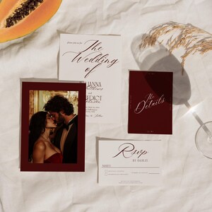 May include: Wedding invitation suite featuring a photo of a couple kissing, a details card, and a RSVP card. The invitation cards have elegant calligraphy. A slice of papaya and a glass of water are also in the image.