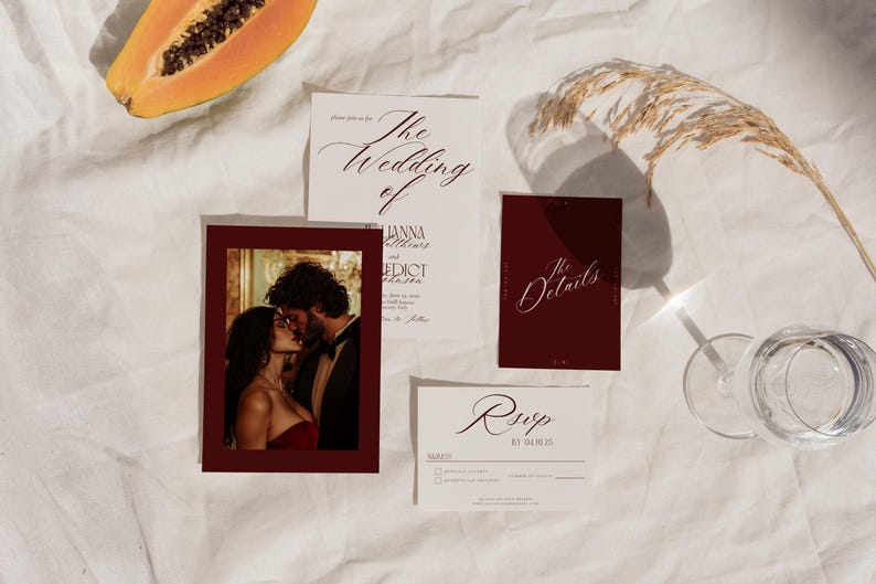 May include: Wedding invitation suite featuring a photo of a couple kissing, a details card, and a RSVP card. The invitation cards have elegant calligraphy. A slice of papaya and a glass of water are also in the image.