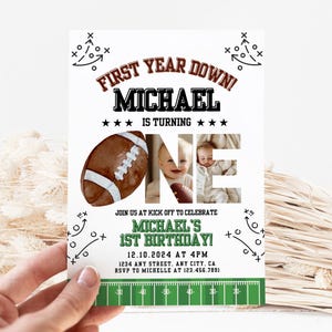Peut inclure: Une invitation blanche sur le thème du football. Le texte indique "First Year Down!" et "Michael fête son premier anniversaire". Comprend un ballon de football et une photo d'un bébé. Le bas présente un graphique de terrain vert et les détails de l'événement.