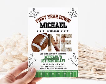 Op de afbeelding: Een witte uitnodigingskaart met een voetbalthema. De tekst luidt "First Year Down!" en "Michael wordt één." Bevat een voetbalafbeelding en een foto van een baby. De onderkant heeft een groene veldafbeelding en evenementdetails.