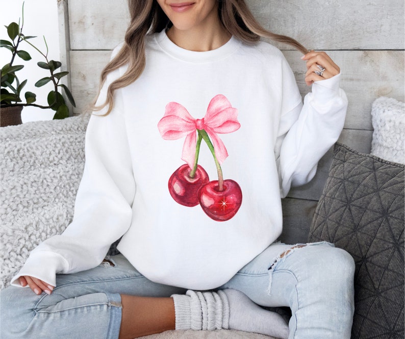 May include: White sweatshirt with a pink bow and two red cherries printed on the front.
