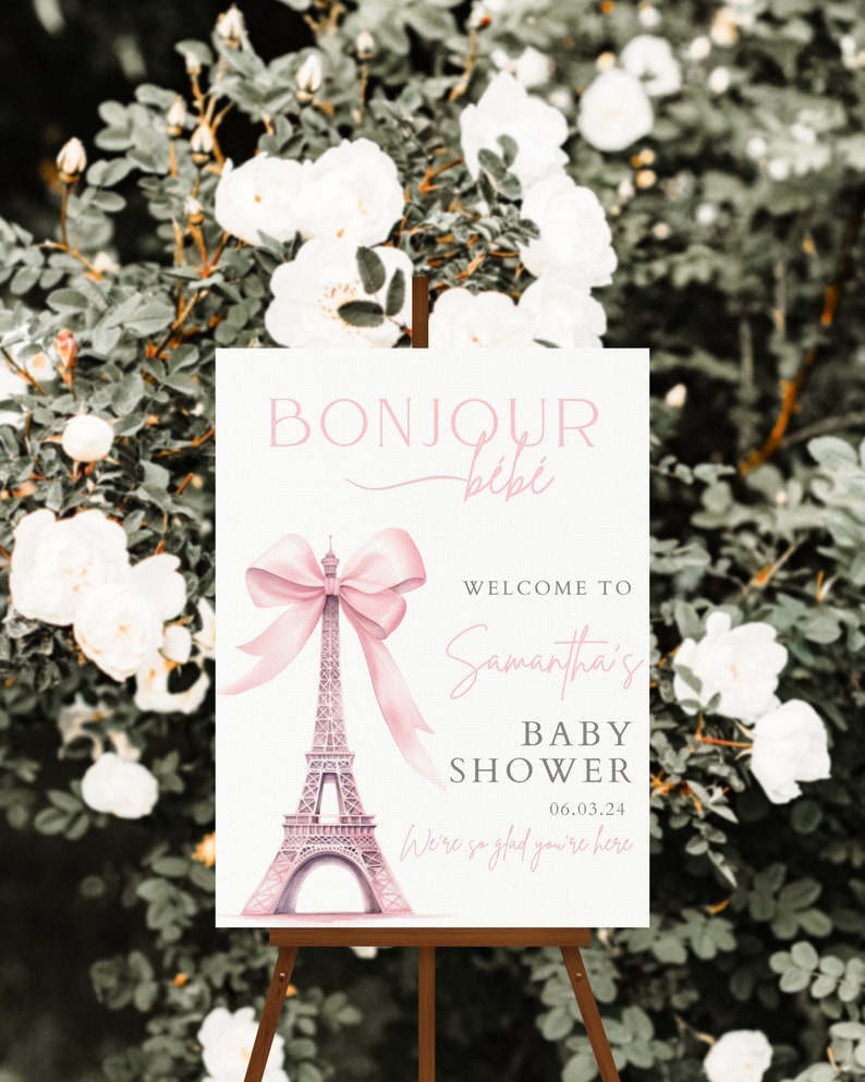 Puede incluir: Un cartel de bienvenida blanco con texto rosa y un lazo rosa en la parte superior de una Torre Eiffel rosa. El texto dice "Bonjour b&eacute;b&eacute;", "Bienvenido al Baby Shower de Samantha", y "06.03.24". El cartel tambi&eacute;n dice "Estamos encantados de que est&eacute;s aqu&iacute;".