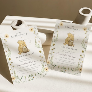 May include: Two baby shower invitations with a Winnie the Pooh theme. Each invitation features a cartoon bear holding a honey pot, surrounded by floral and bee illustrations. The text reads "our little honey" and "Is on the Way!"