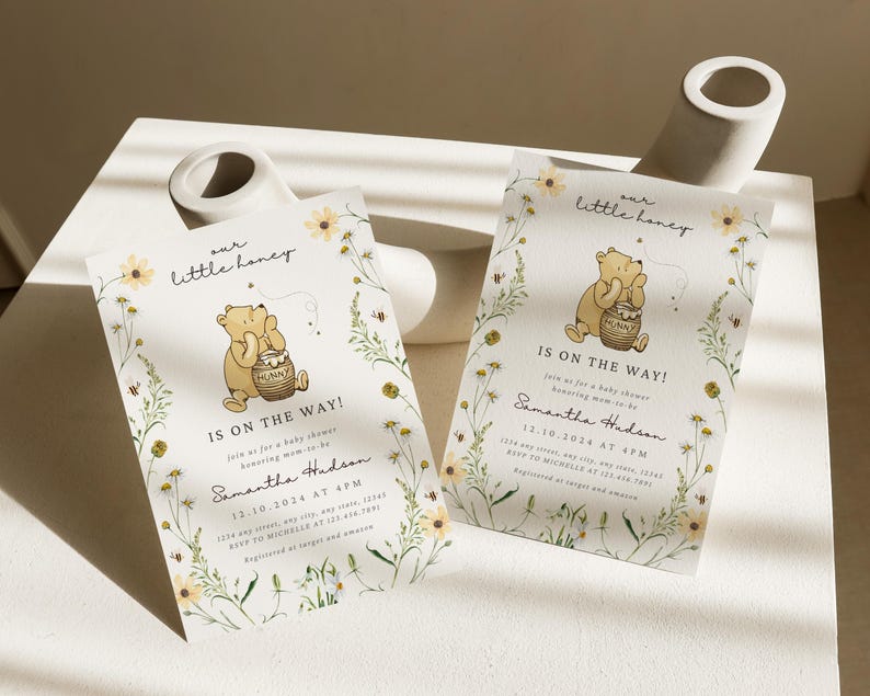 May include: Two baby shower invitations with a Winnie the Pooh theme. Each invitation features a cartoon bear holding a honey pot, surrounded by floral and bee illustrations. The text reads "our little honey" and "Is on the Way!"