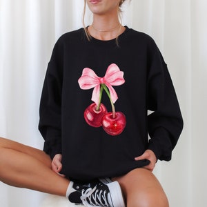 May include: Black sweatshirt with a pink bow and two red cherries printed on the front.