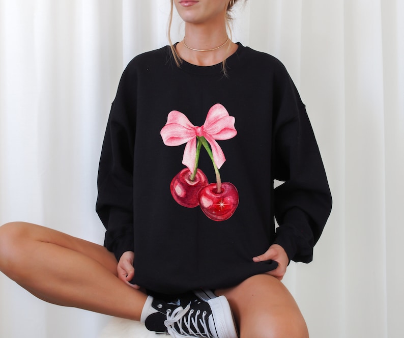 May include: Black sweatshirt with a pink bow and two red cherries printed on the front.