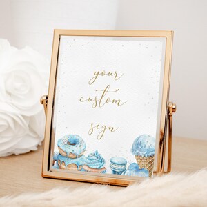 May include: Gold framed sign with the text "your custom sign" in gold lettering. The sign features watercolour illustrations of blue doughnuts, a blue ice cream cone, and blue macarons.