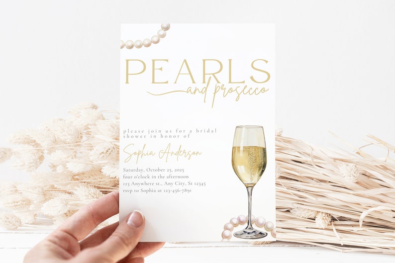 May include: A white bridal shower invitation with gold text that reads "PEARLS and prosecco". The invitation features a glass of champagne and a string of pearls. The text also includes the bride's name, the date, time, and location of the shower.
