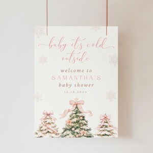 May include: A pink and white baby shower sign with the text "baby it's cold outside" and "welcome to Samantha's baby shower 12.10.2024". The sign features three watercolor illustrations of Christmas trees with pink bows.