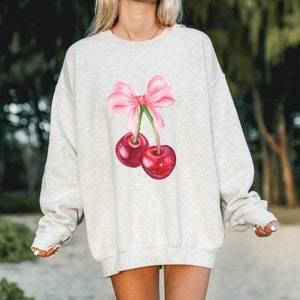 May include: A gray sweatshirt with a pink bow and two red cherries printed on the front.