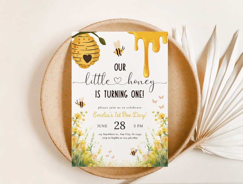 May include: A yellow and white invitation card with a beehive, bees, and flowers. The text reads "Our little honey is turning one!" and includes the date and time of the event.