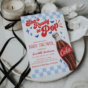 Puede incluir: Invitaci&oacute;n a un baby shower con el texto "She's Ready to Pop" en rojo y azul. La invitaci&oacute;n presenta una ilustraci&oacute;n de una botella de cola y detalles del evento, incluyendo la fecha, hora y lugar.