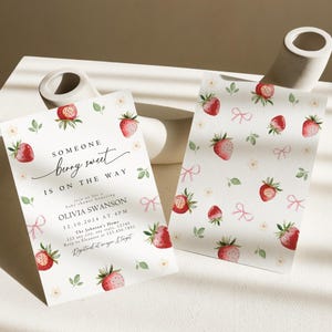 May include: A baby shower invitation with a strawberry theme. The invitation is white with pink and green accents. The text on the invitation reads "Someone berry sweet is on the way." The invitation also includes the name Olivia Swanson, the date 12.10.2024, and the time 4PM. The invitation is decorated with strawberries and bows.