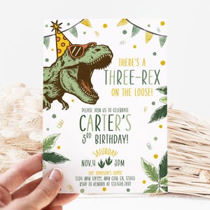 May include: A birthday invitation featuring a green dinosaur wearing sunglasses and a party hat. The text reads "There's a Three-Rex on the Loose!" and invites guests to Carter's 3rd birthday on November 4th at 3 PM. The invitation includes the address and RSVP information.