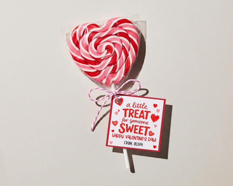 May include: A heart-shaped lollipop with red and pink swirls, wrapped in clear cellophane. A small tag reads "a little TREAT for someone SWEET Happy Valentine's Day! From Olivia" tied with pink and white string.