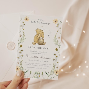 May include: Baby shower invitation featuring a Winnie the Pooh illustration with the text "our little honey is on the way!". The invitation is decorated with floral elements and includes event details. An envelope with a wax seal is also present.