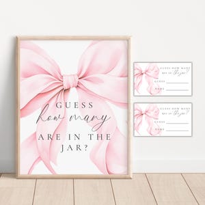 May include: A framed print and two smaller cards with a pink bow design. The framed print reads "GUESS how many ARE IN THE JAR?" in elegant script. The cards have space for guesses and names, with the text "GUESS HOW MANY are in the jar?"