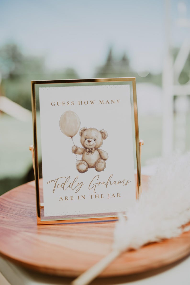 May include: A framed sign with gold trim, featuring a watercolor illustration of a teddy bear holding a balloon. The sign reads "Guess How Many" and "Teddy Grahams are in the jar."