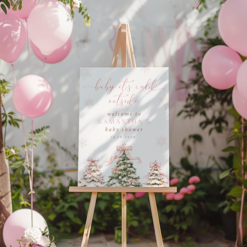 May include: A white sign with pink text that reads "baby it's cold outside, welcome to Samantha's baby shower 12.10.2014". The sign is decorated with snowflakes and three watercolor illustrations of Christmas trees with pink bows.