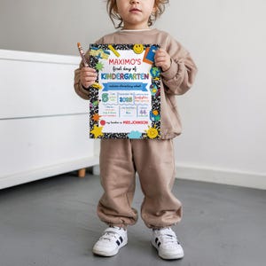 K&ouml;nnte beinhalten: Ein Kind h&auml;lt ein farbenfrohes Schild mit der Aufschrift "MAXIMO'S first day of KINDERGARTEN". Das Schild hat einen schwarz-wei&szlig;en Hintergrund mit schulischen Grafiken. Das Schild enth&auml;lt das Datum, das Alter und den Namen des Lehrers.