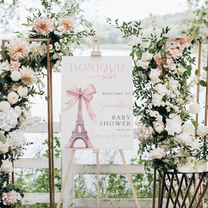 Puede incluir: Un cartel blanco con un lazo rosa y un gr&aacute;fico de la Torre Eiffel. El cartel dice "Bonjour b&eacute;b&eacute;" y "Bienvenido al Baby Shower de Samantha 06.03.24 Estamos encantados de que est&eacute;s aqu&iacute;".