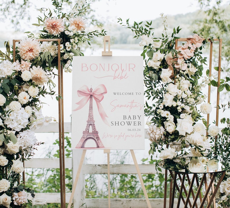 Puede incluir: Un cartel blanco con un lazo rosa y un gr&aacute;fico de la Torre Eiffel. El cartel dice "Bonjour b&eacute;b&eacute;" y "Bienvenido al Baby Shower de Samantha 06.03.24 Estamos encantados de que est&eacute;s aqu&iacute;".