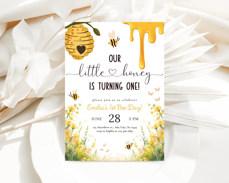May include: A yellow and white bee-themed first birthday party invitation with a beehive, dripping honey, and the text "Our little honey is turning one!"  Please join us to celebrate Emilia's 1st Bee-Day! June 28, 3 PM, 123 Anywhere st., Any City, St 12345, rsvp to Sophia at 123-456-7891.
