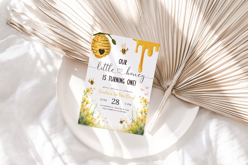 May include: A yellow and white bee-themed first birthday party invitation with a beehive, dripping honey, and the text "Our little honey is turning one!"  Please join us to celebrate Emilia's 1st Bee Day! June 28, 3 PM.