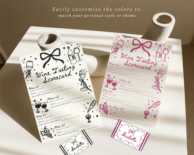 Pu&ograve; includere: Due schede di valutazione della degustazione di vini con illustrazioni di fiocchi e calici. Uno &egrave; in bianco e nero, l'altro rosa. Il testo "Wine Tasting Scorecard" &egrave; in alto. Piccole carte con il nome "Isabella" in basso.