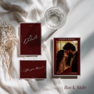 May include: A set of three rectangular wedding stationery cards in deep burgundy with white borders. One card features a photograph of a couple with the text Julianna & Benedict. Another card displays the text The Details, and the third says See you there?