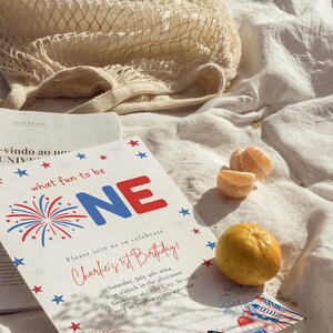 May include: A white invitation card with red, white, and blue stars and fireworks. The text on the card reads "what fun to be ONE" and "Charlie's 1st Birthday!" with details about the party date, time, and location.