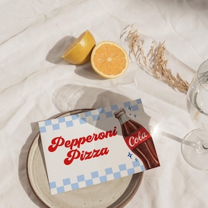 Może przedstawiać: Martwa natura z talerzem z kartą z napisem "Pepperoni Pizza" i ilustracją butelki coli. Karta ma niebiesko-biały wz&oacute;r w kratkę. Obecne są r&oacute;wnież dwie poł&oacute;wki cytryny i szklanka.